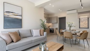 A modern living room with a grey sofa, a wooden coffee table, and a dining area with a round table and chairs. - GG Villas Falassarna (Chania)