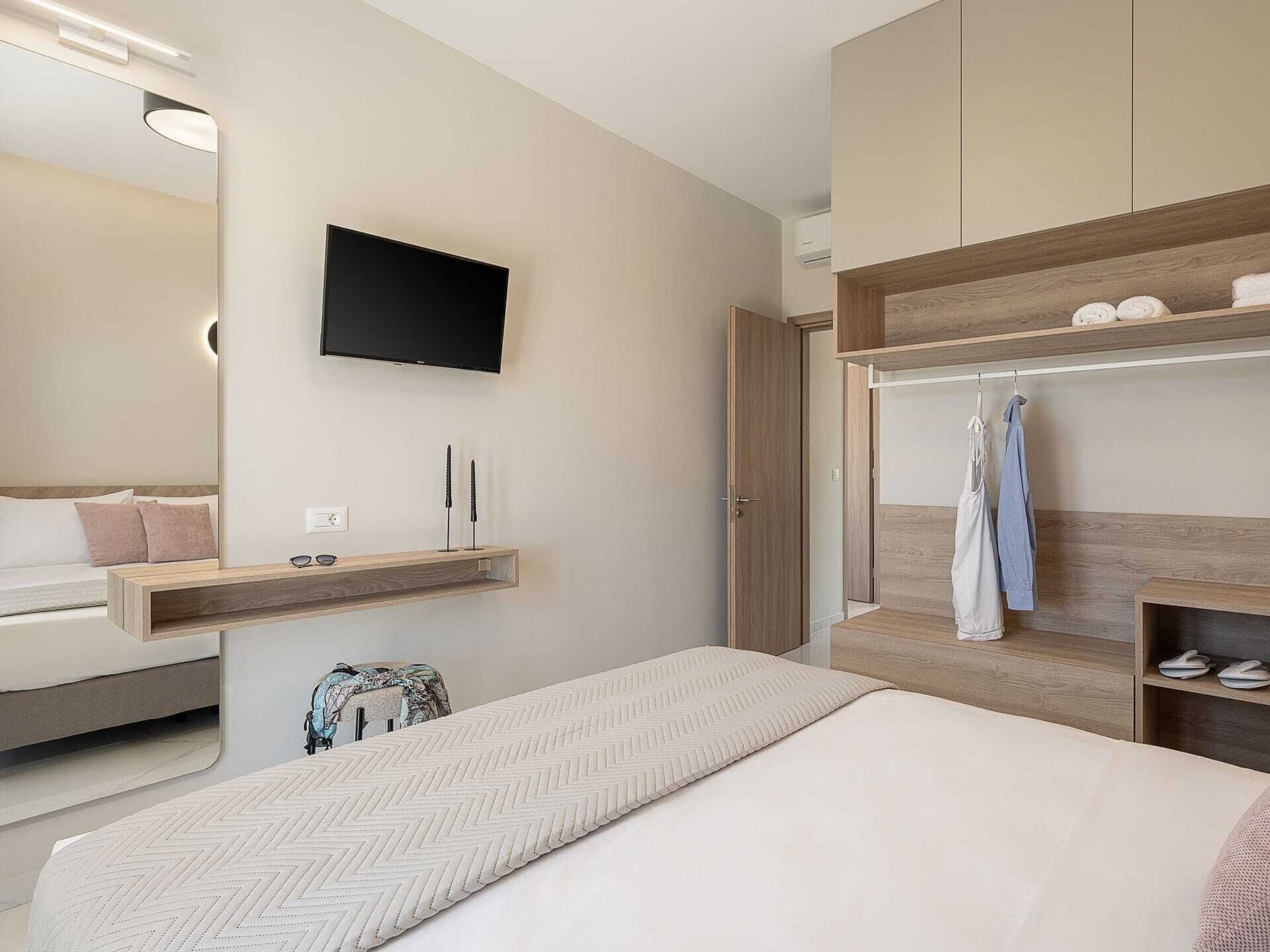 Une chambre moderne avec un lit, un téléviseur fixé au mur, une armoire en bois et un meuble à chaussures intégré.