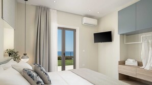 A modern bedroom with a bed, a TV, a balcony with a view, and a bathroom with a mirror and towel rack. - GG Villas Falassarna (Disability Access) (Chania)