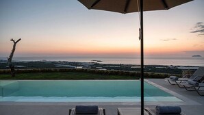 An infinity pool with a view of the ocean at sunset, lounge chairs, and a table with a towel. - GG Villas Falassarna (Disability Access) (Chania)