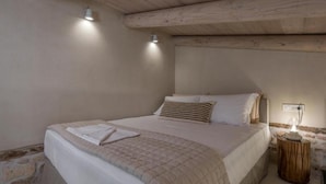 A bedroom with a bed, a bedside table, and a wall-mounted light fixture. - Il Campanile Suite for Two (Crete)