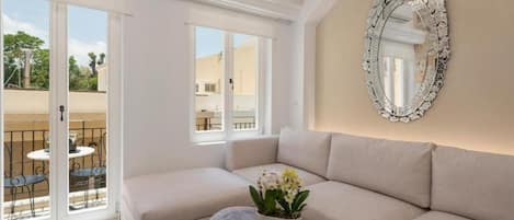 A room with a beige sofa, a wooden coffee table with a plant, and a large ornate mirror on the wall.