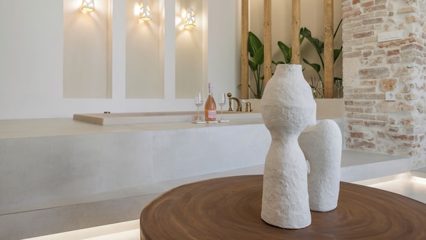 A modern interior with a round wooden table, a white sculptural piece, and a brick wall. - Il Campanile Suite for Two (Crete)