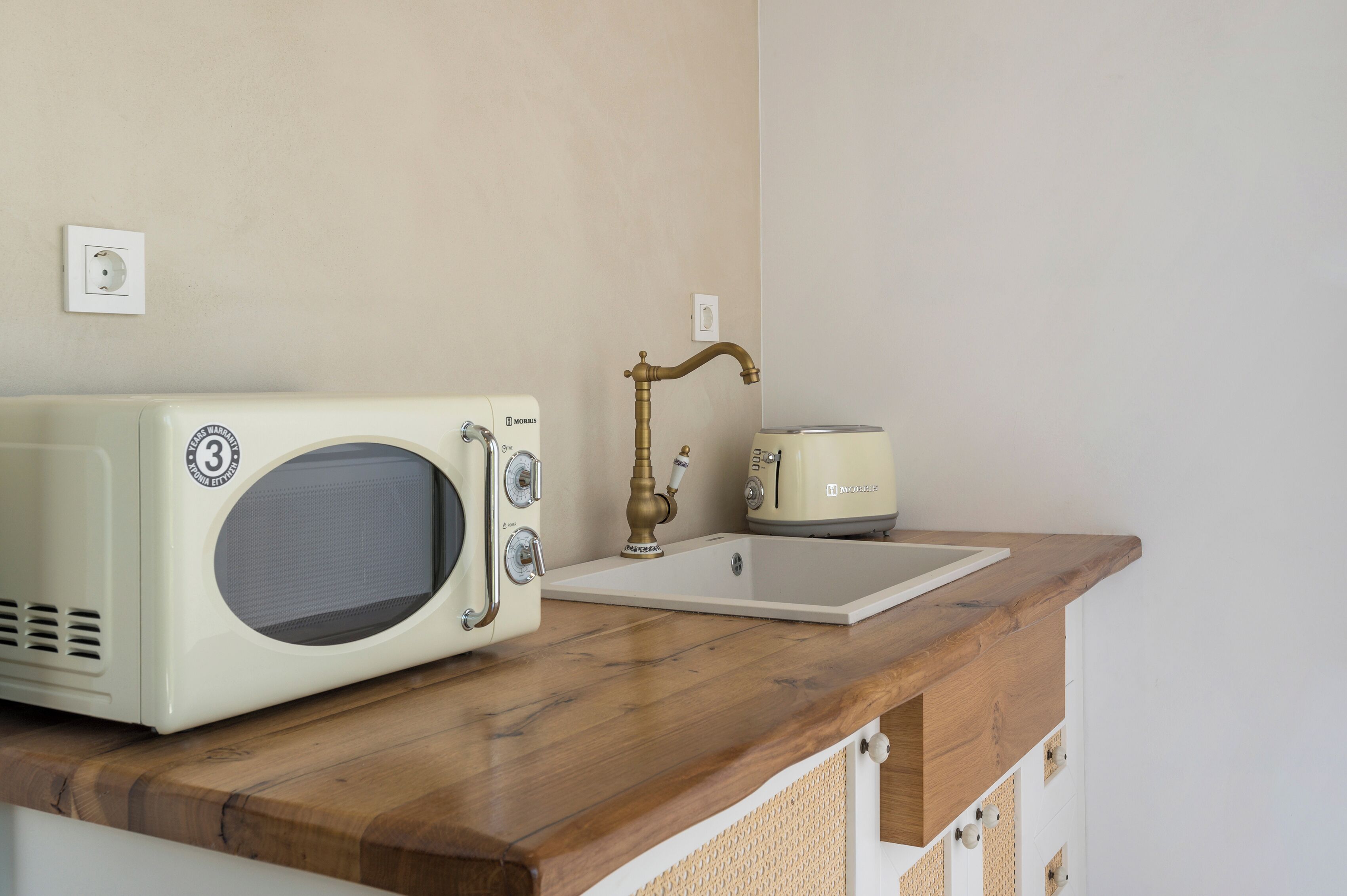 A kitchenette with a vintage-style microwave, a toaster, and a sink with a brass faucet.