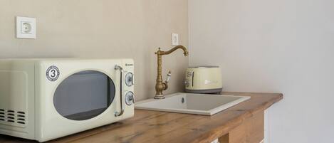 A kitchenette with a vintage-style microwave, a toaster, and a sink with a brass faucet.