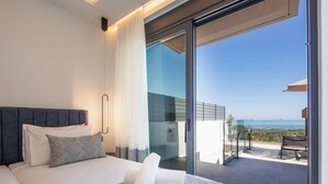 Una habitación de hotel moderna con una cama grande, un balcón con vista al mar y un ventanal de vidrio que da al balcón.