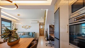 A modern kitchen with a built-in oven, a dining area with a wooden table and chairs, and a living area with a sofa and decorative wall art. - Horizon West Villa │Private Pool, Secluded Luxury Modern Villa (Chania)