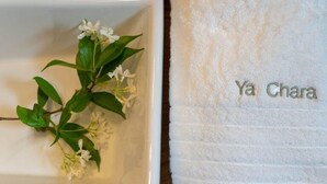 Un baño blanco con una toalla blanca que dice "Ya Chara" y una rama con flores blancas.