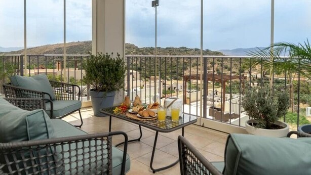 Un balcón con mobiliario de mimbre, una mesa con comida y bebidas, y vistas a un paisaje montañoso.