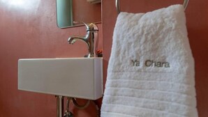Un baño con un lavamanos blanco, un espejo y una toalla colgada en un perchero de metal con el texto 