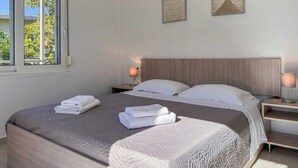 A neatly made bed with white linens, two bedside tables with lamps, and a window with a view of greenery. - Villa Adam: Tranquility and Luxury with a Poolside View (Crete)