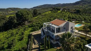 A modern two-story house with a flat roof, surrounded by lush greenery and hills. - Villa Adam: Tranquility and Luxury with a Poolside View (Crete)