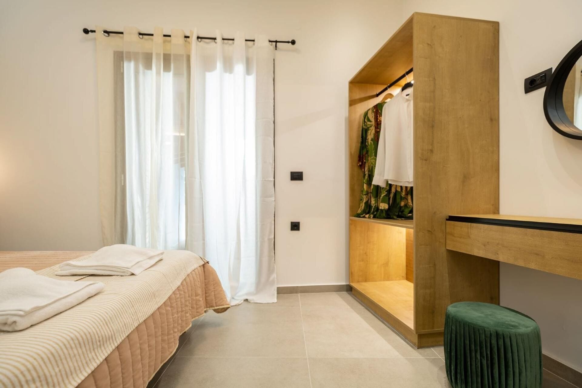 A bedroom with a bed, a wooden wardrobe, a green stool, and a window with curtains.