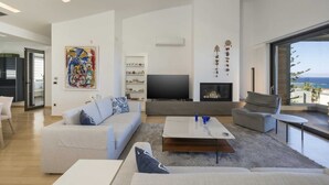 A spacious living room with a large TV, a fireplace, and a view of the ocean. - Modern villa w/pool, near beach & city centre (Crete)