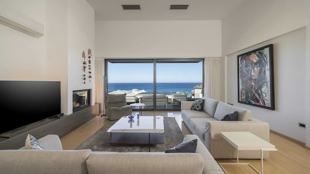 A modern living room with a large TV, sofas, a coffee table, and a view of the sea. - Modern villa w/pool, near beach & city centre (Crete)
