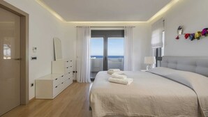 A modern bedroom with a large bed, a dresser, a mirror, and a view of the sea through the window. - Modern villa w/pool, near beach & city centre (Crete)