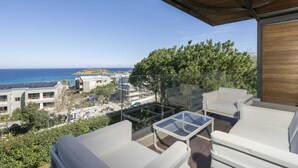 A balcony with white furniture, a glass table, and a view of the sea and buildings. - Modern villa w/pool, near beach & city centre (Crete)