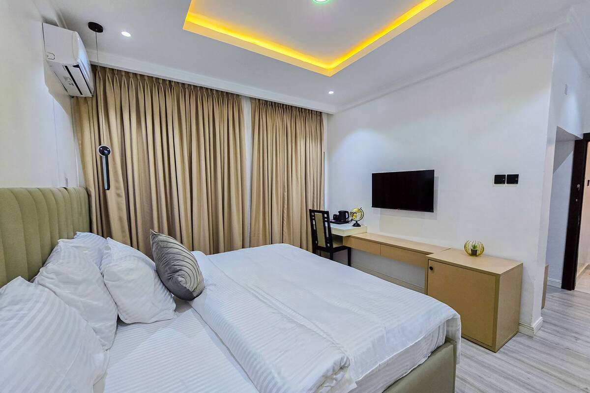A hotel room with a bed, a desk, a TV, and an air conditioning unit.