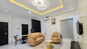 A modern living room with a sofa, armchair, and a coffee table, featuring a patterned rug and recessed ceiling lighting. - Twinny Hotels & Suites (Lagos)