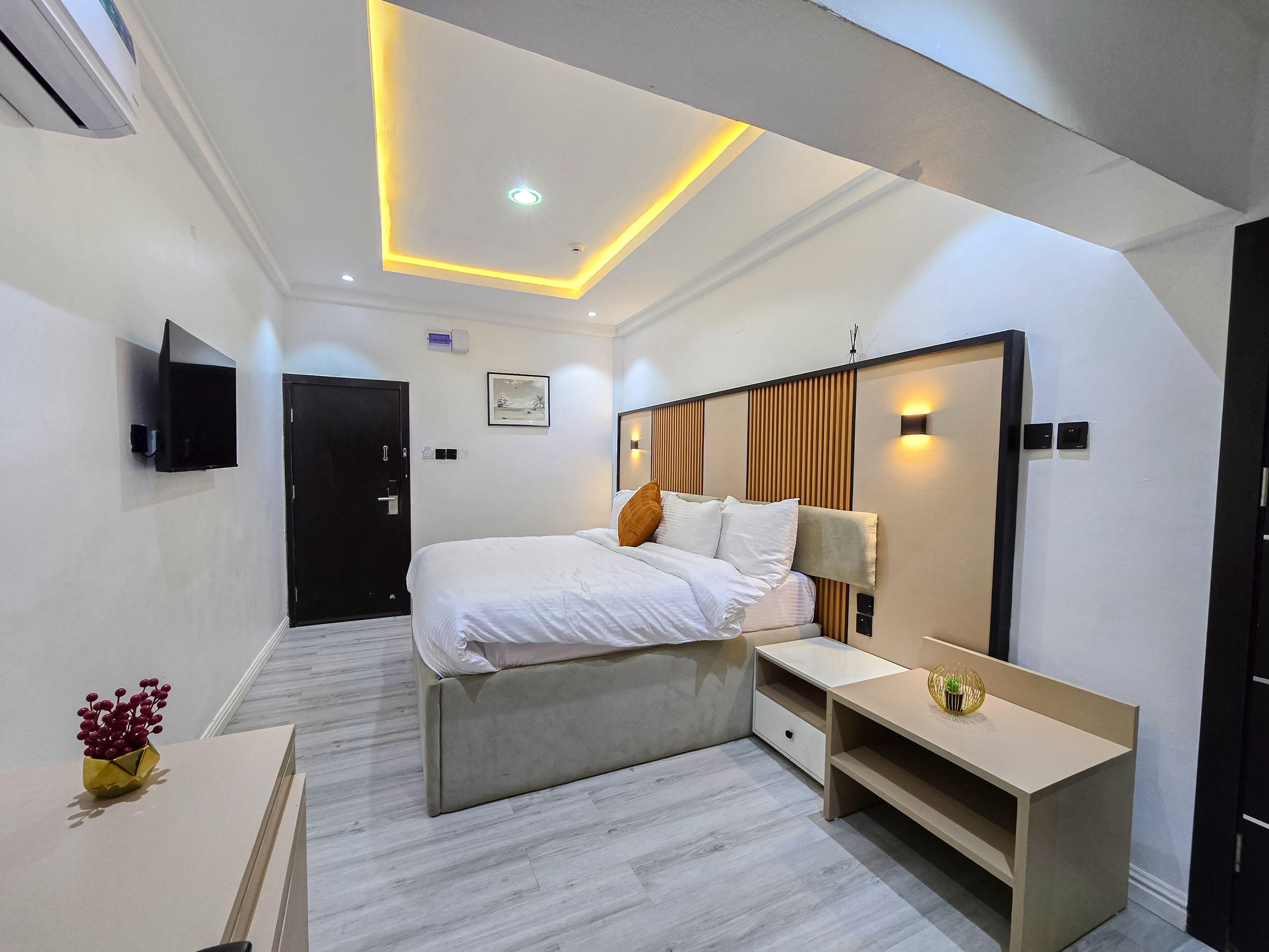 A modern hotel room with a bed, bedside table, and a TV mounted on the wall.