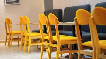 A row of yellow chairs with wooden frames and yellow cushions, arranged in a dining area with a tiled floor.