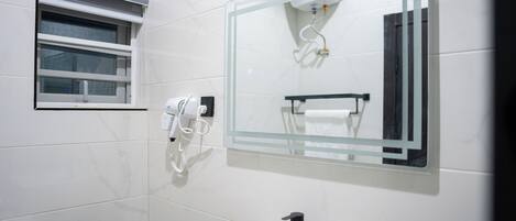 Un baño con lavamanos blanco, grifo negro, cabina de ducha de vidrio y un perchero para toallas.