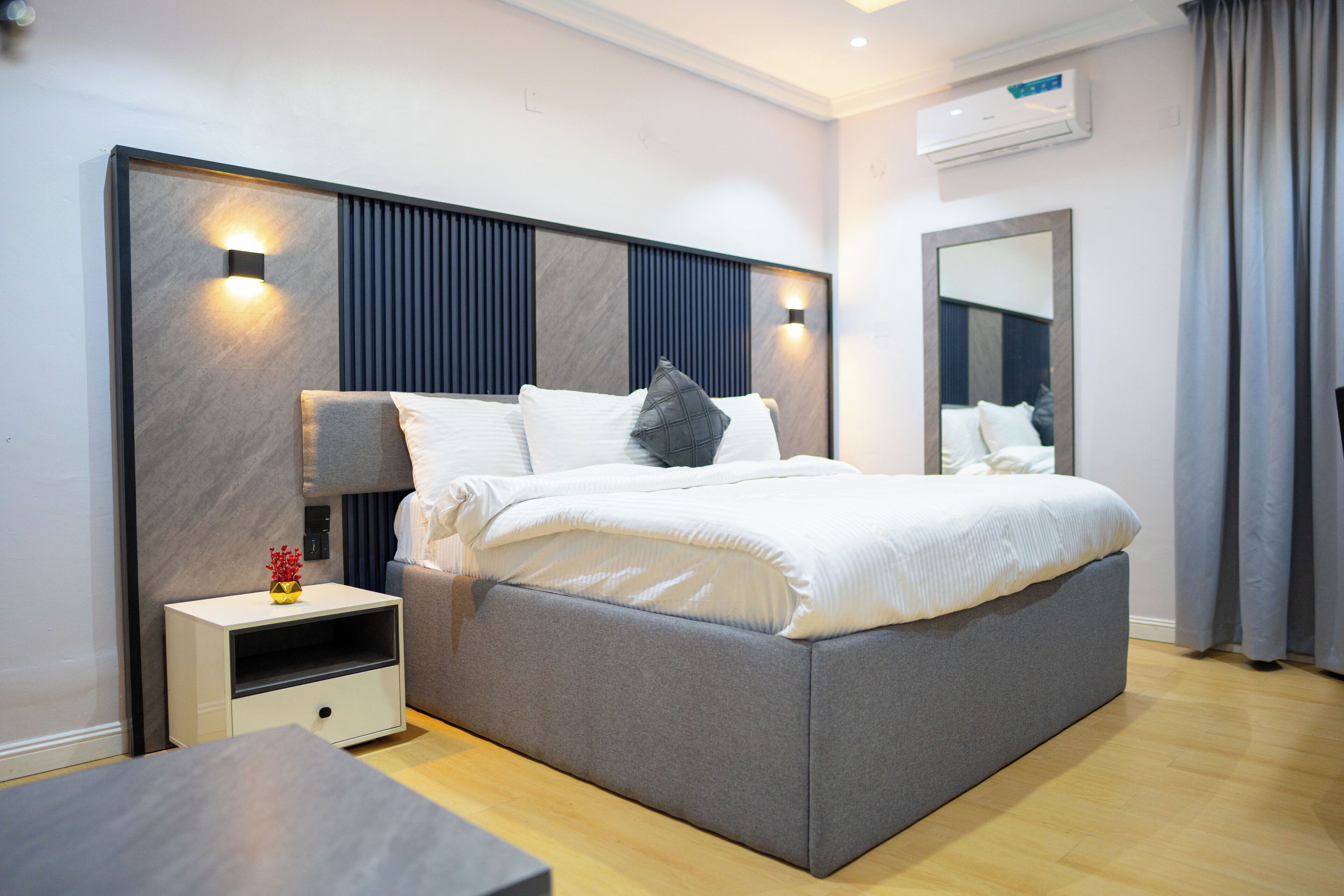 A modern bedroom with a large bed, bedside tables, a nightstand, and a mirror.