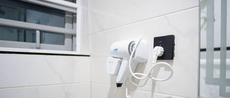 Un sèche-cheveux fixé sur un mur recouvert de carreaux blancs, avec une fenêtre au-dessus.
