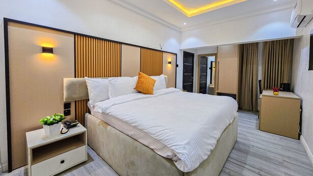 A modern hotel room with a large bed, bedside table, and a small desk with a chair. - Twinny Hotels & Suites (Lagos)