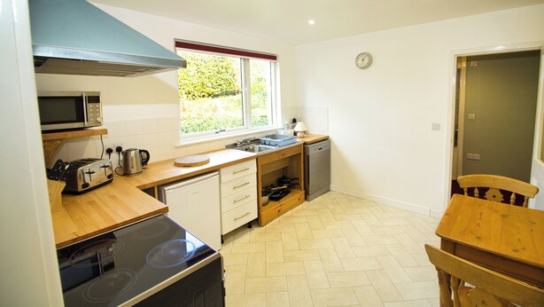 A compact kitchen with a microwave, toaster, and stove, wooden countertops, a window with a view, and a dining area with a chair. - Accessible Bungalow - 4 Beds 2 Baths -dog Friendly (Berwick-upon-Tweed)