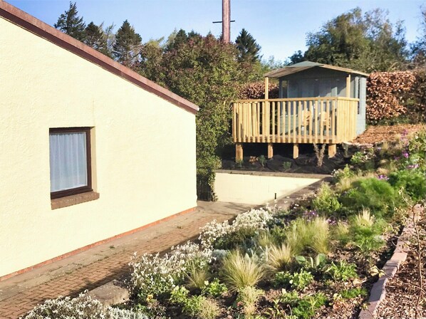 A building with a small balcony, a window, and a garden with various plants. - Accessible Bungalow - 4 Beds 2 Baths -dog Friendly (Berwick-upon-Tweed)