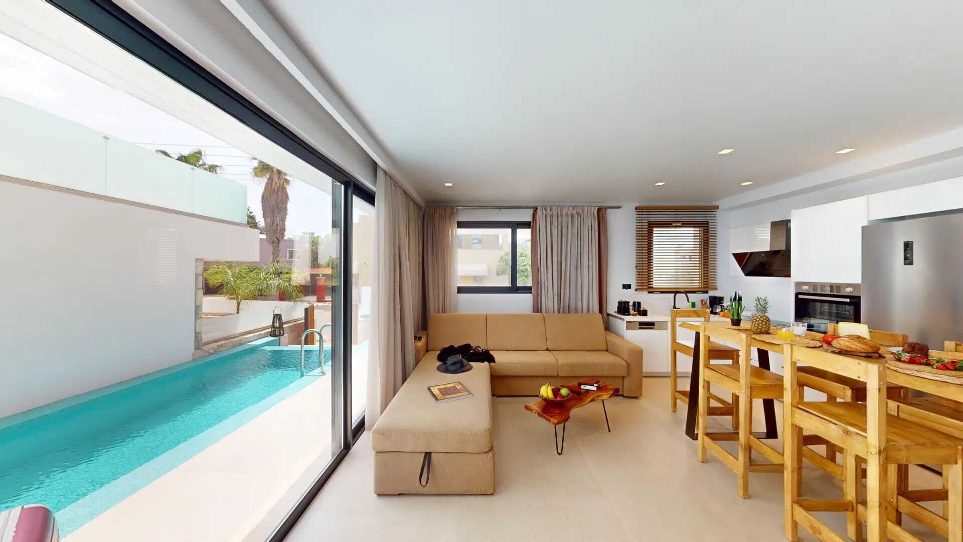 A modern living area with a pool, a sofa, a dining table, and a kitchen.
