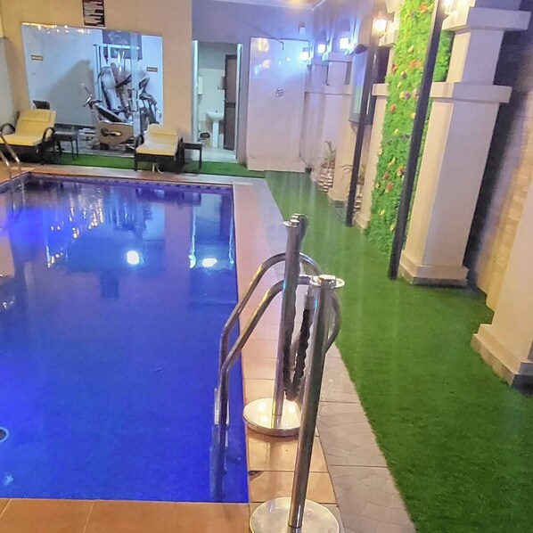 A swimming pool with a metal safety rail, surrounded by a green artificial lawn and white pillars. - Morning Side Boutique Hotel and Suites  (Lagos)