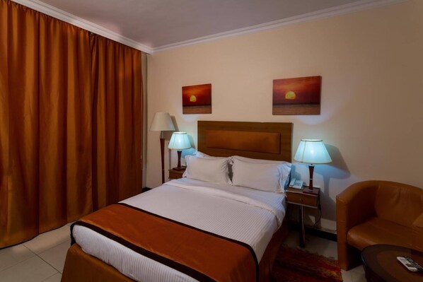 A hotel room with a large bed, two bedside tables with lamps, a chair, and two paintings on the wall. - Morning Side Boutique Hotel and Suites  (Lagos)