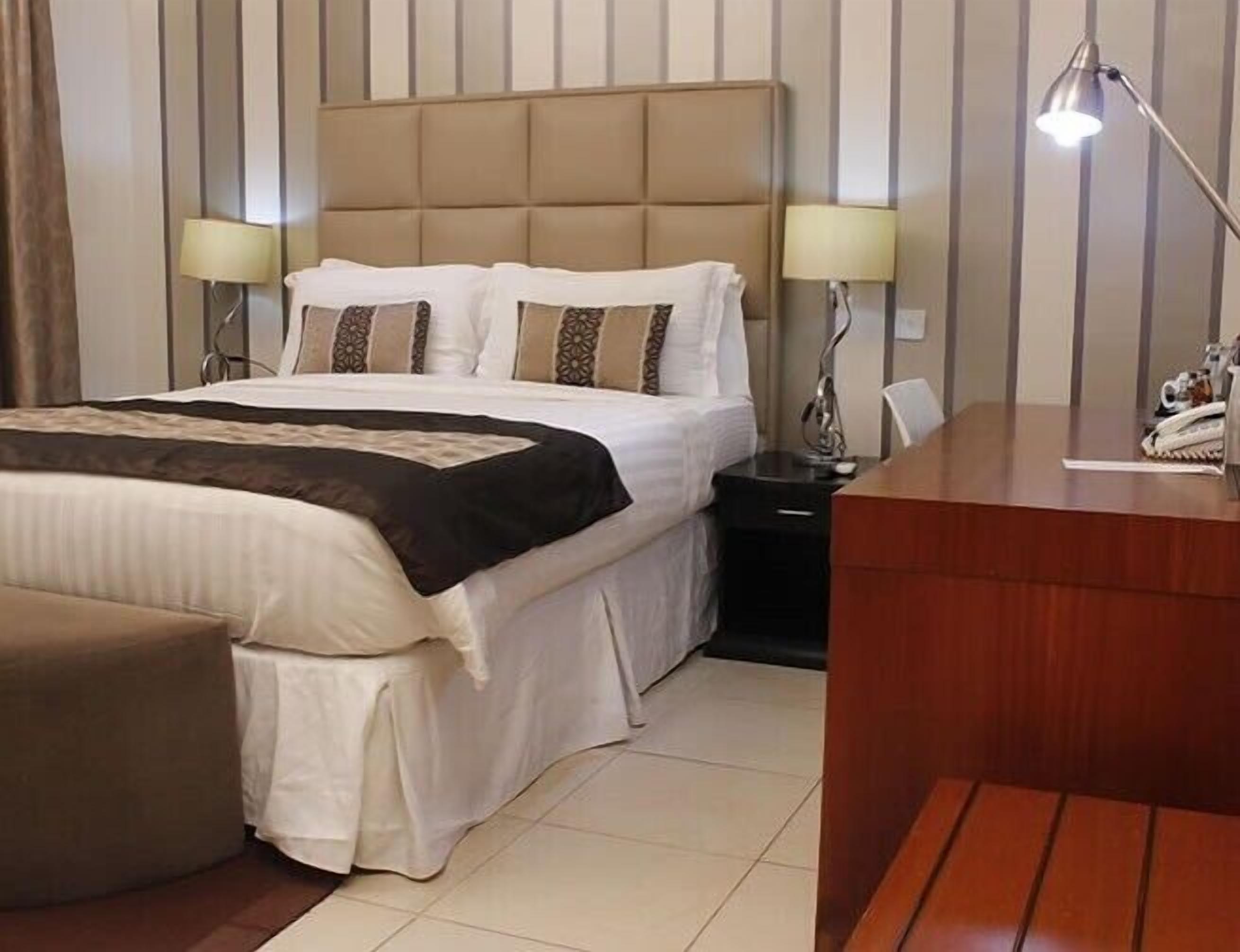 A hotel room with a bed, bedside tables, a desk, and a chair.