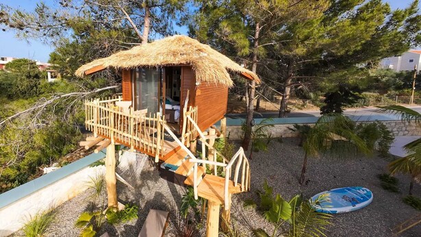 Una casa en árbol de madera con techo de paja, una escalera de madera y una pequeña terraza.