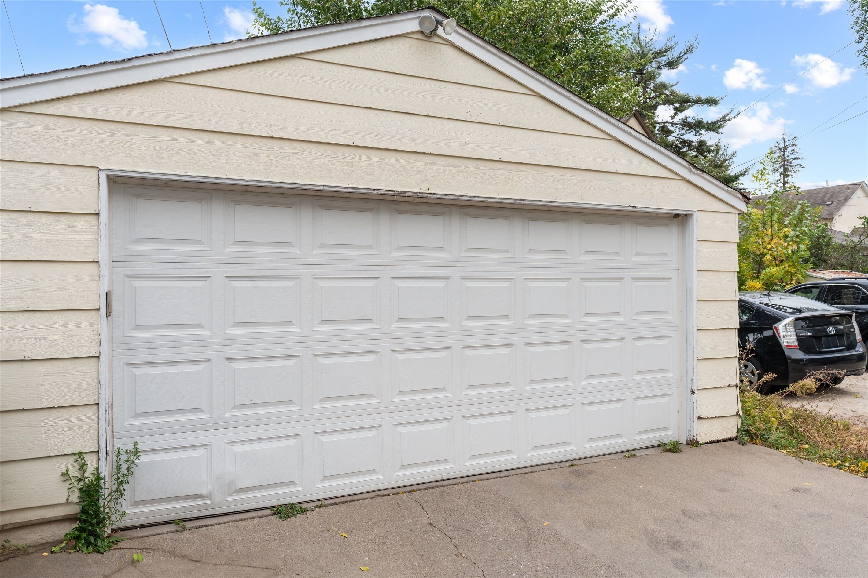 Un garage avec une porte blanche, une allée en béton et un véhicule noir garé devant.