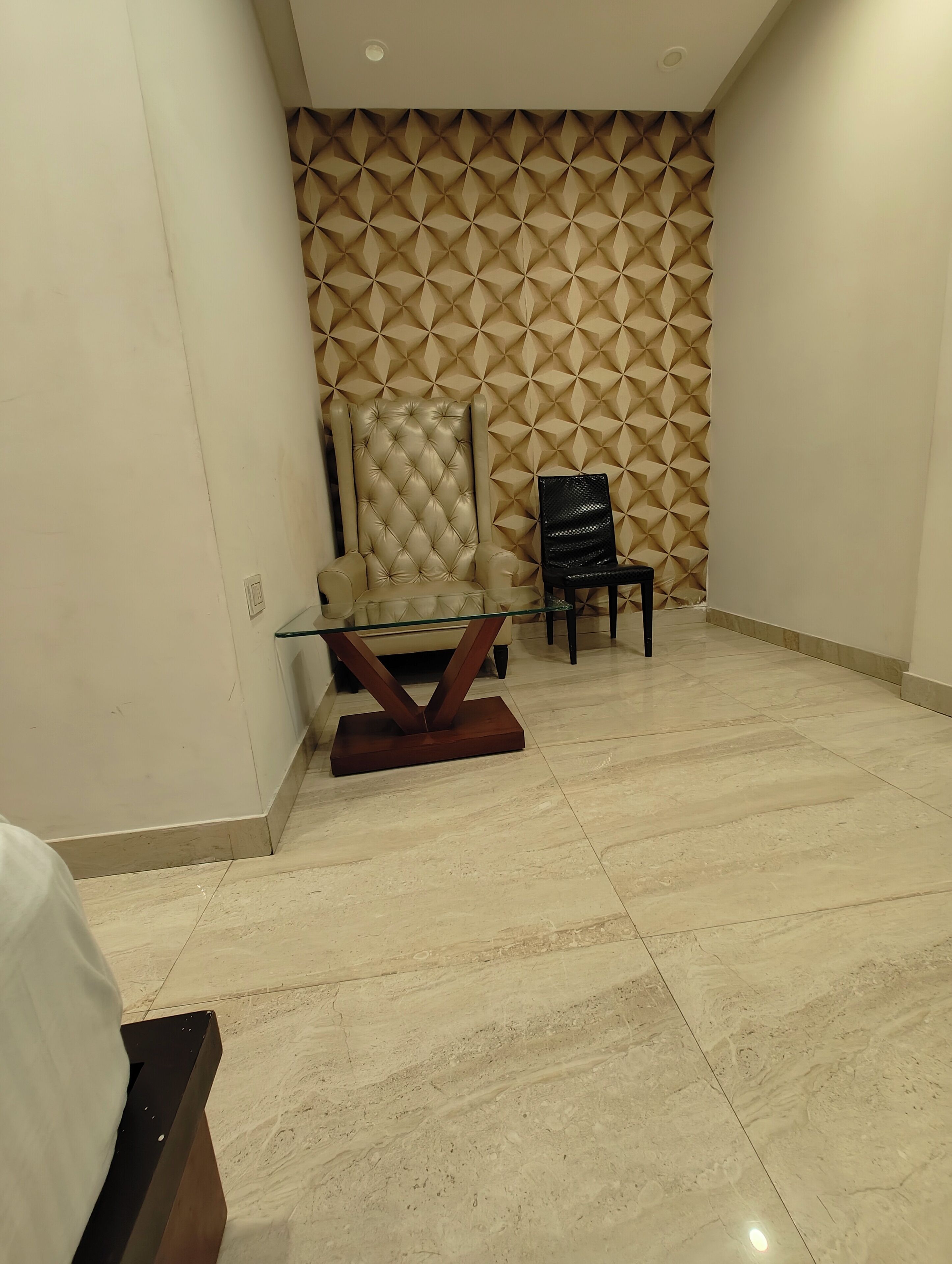A room with a marble floor, a glass table with a wooden base, a beige upholstered chair, and a black chair.