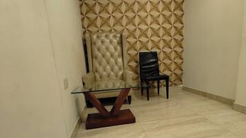 A room with a marble floor, a glass table with a wooden base, a beige upholstered chair, and a black chair.