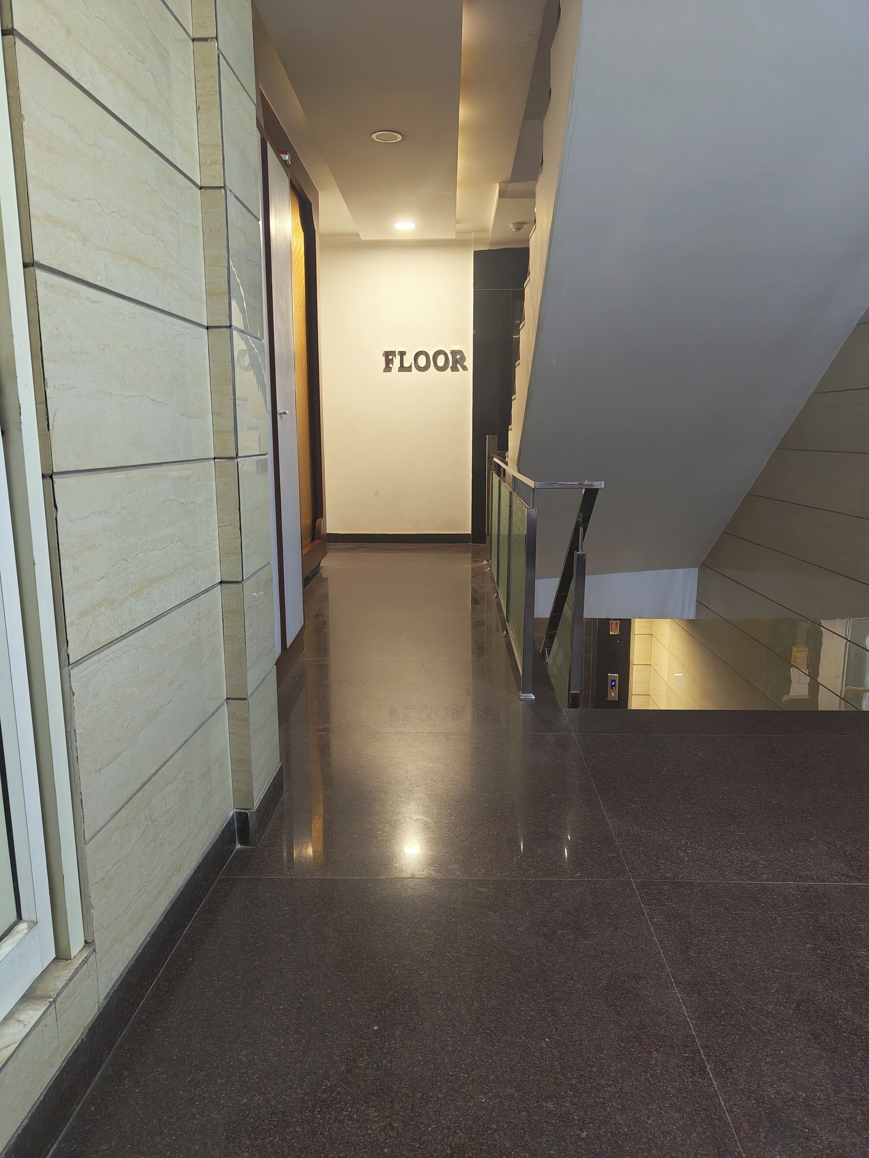 A corridor with a polished floor leading to a staircase. A sign on the wall reads "FLOOR".
