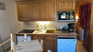 A compact kitchen with wooden cabinets, a microwave, a dishwasher, and a sink. - Apartment foreclosures (Villard-sur-Doron)