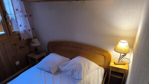 A single bed with white linens, a wooden headboard, a bedside table with a lamp, and a nightstand with a lamp. - Apartment foreclosures (Villard-sur-Doron)