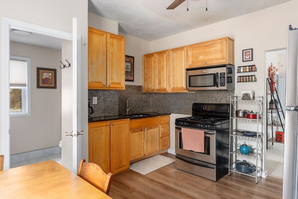 A kitchen with wooden cabinets, a microwave, stove, and a shelf with jars.