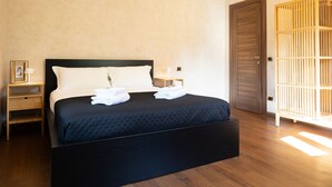 Una cama bien hecha con sábanas blancas, una mesita de noche de madera con lámpara y un armario de madera en una habitación luminosa con suelo de madera.
