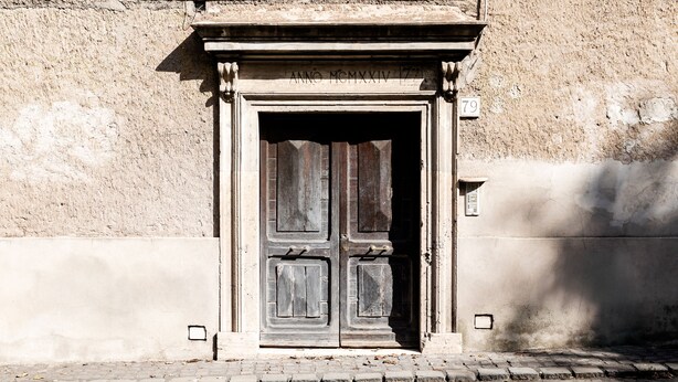 Una puerta de madera desgastada con una placa sobre ella, incrustada en un muro de piedra.