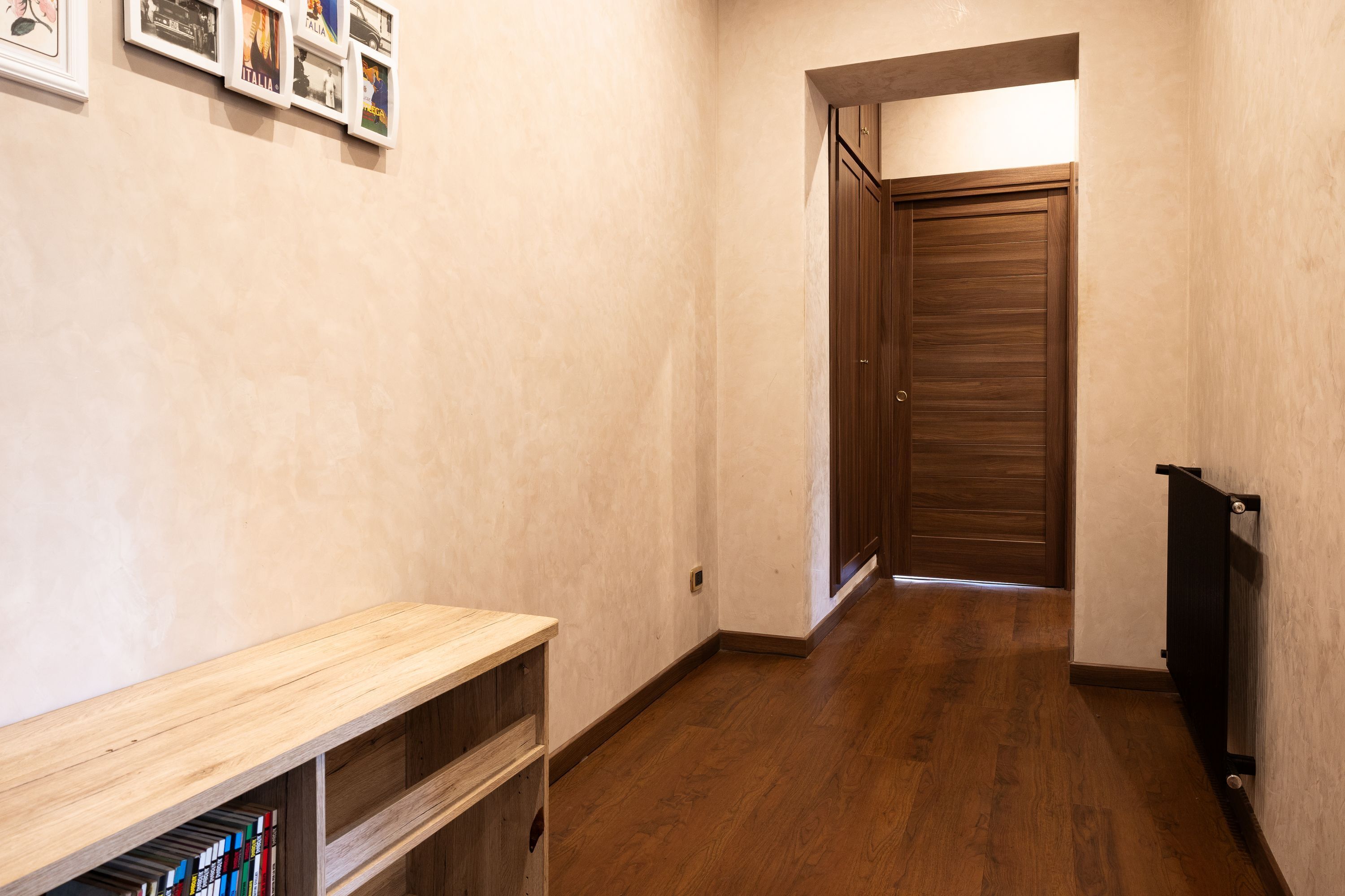 Un couloir avec un plancher en bois, une bibliothèque et une porte au fond.