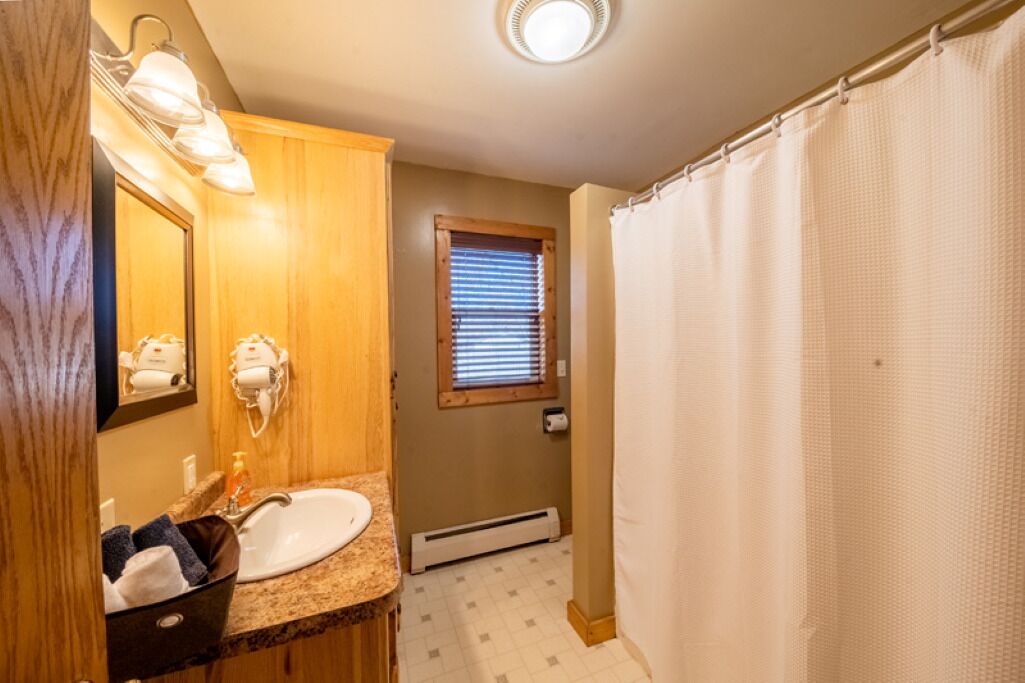 A bathroom with a sink, mirror, towel rack, and a window with blinds.