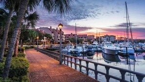 A marina with boats docked, a walkway, and buildings in the background.