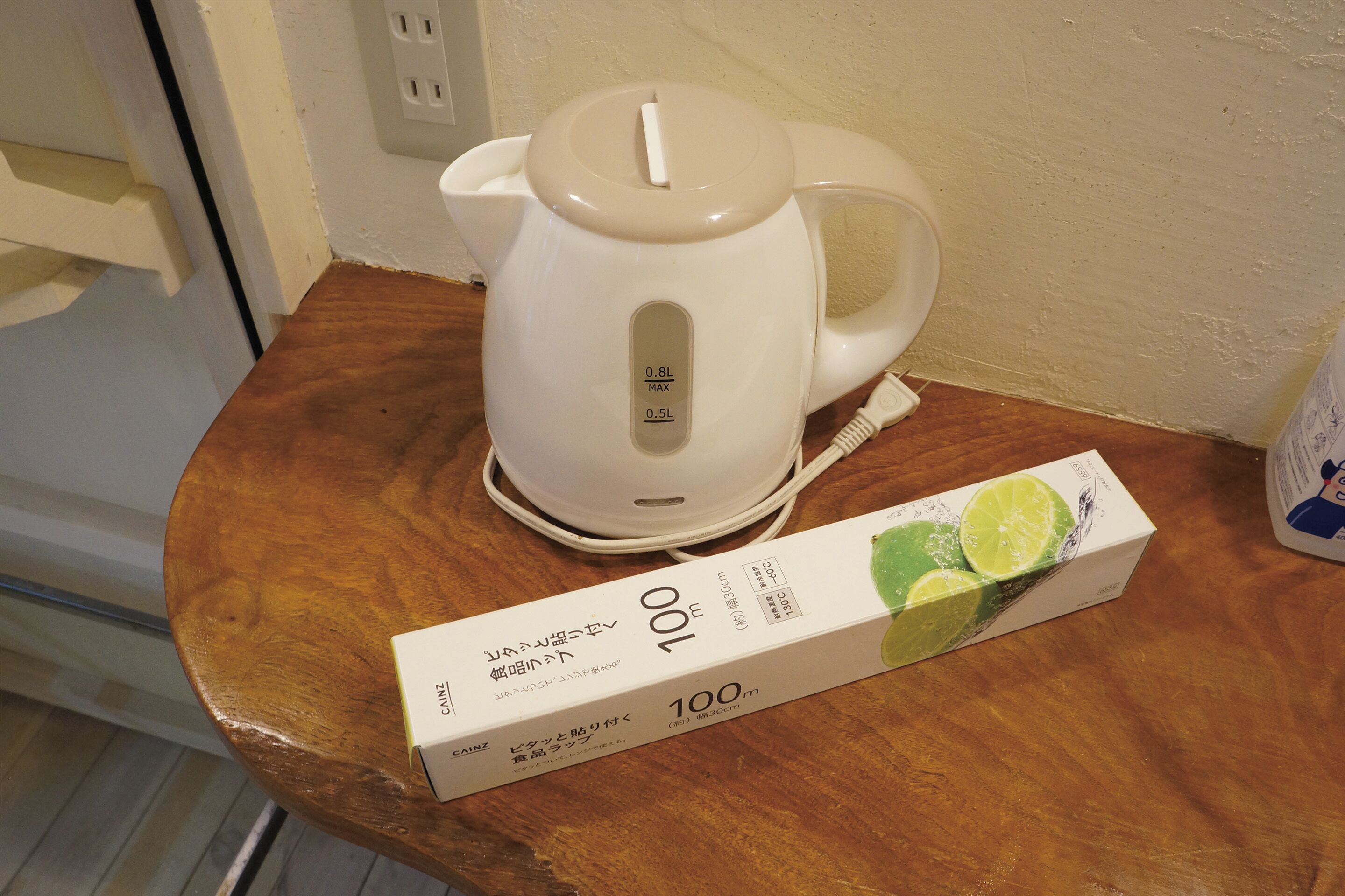 Ein weißes elektrisches Wasserkocher mit digitaler Anzeige auf einem Holztisch. Daneben befindet sich eine Schachtel mit der Aufschrift '100' und japanischem Text.