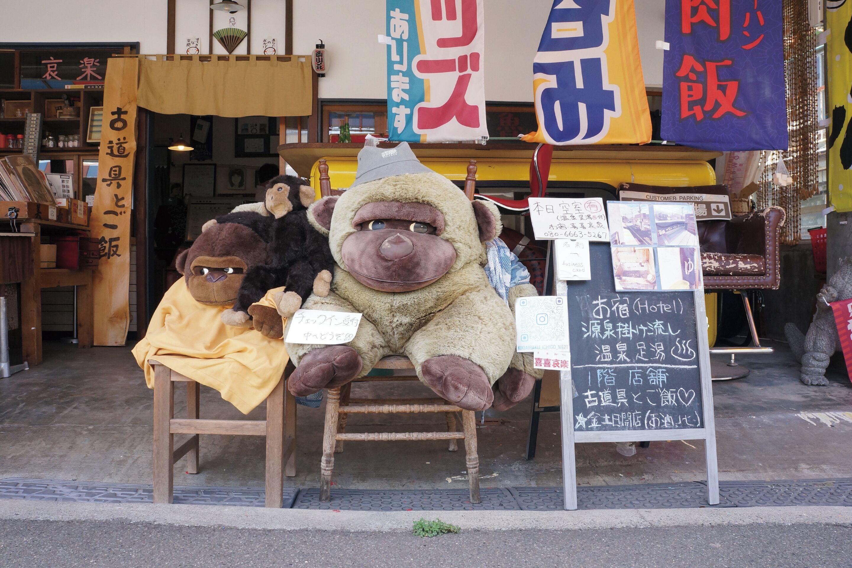 A storefront with a wooden signboard and plush monkey figures.